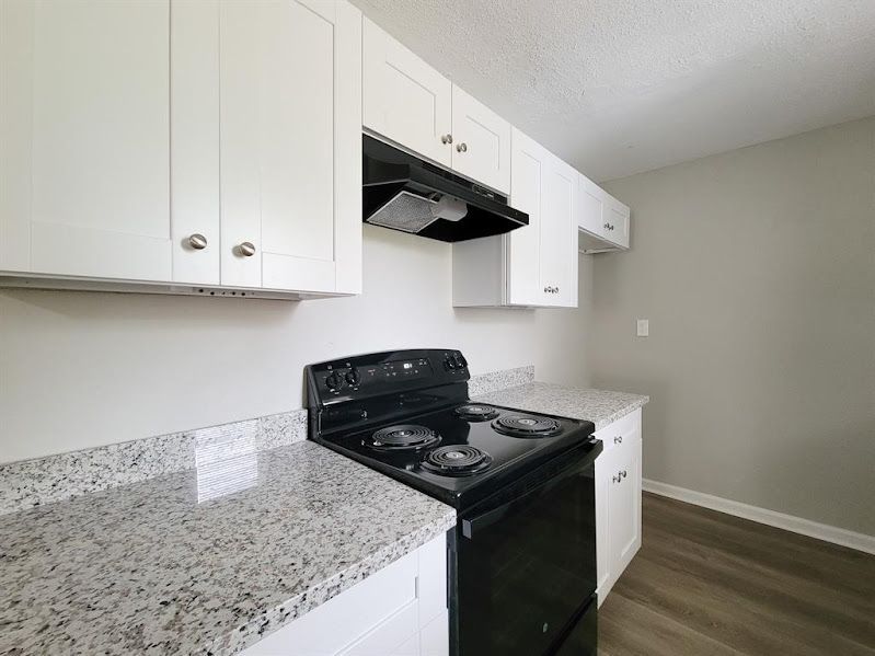 A kitchen with white cabinets , a black stove , and a granite counter top.