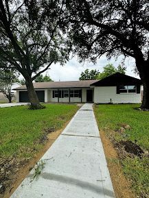 A concrete walkway leading to a house with trees in the background.