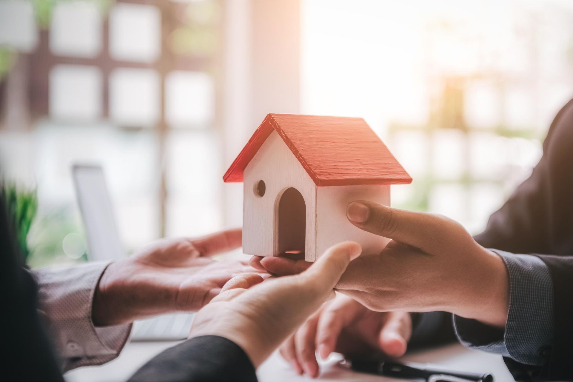 Hands passing a miniature house with a red roof, likely a real estate transaction.