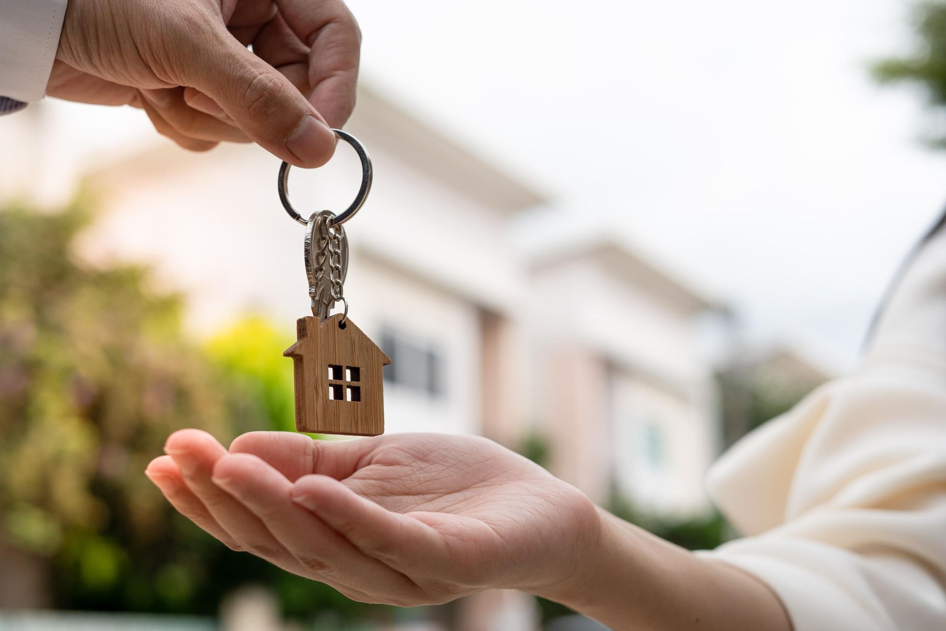 Hand passing house key to another person, outside near homes.