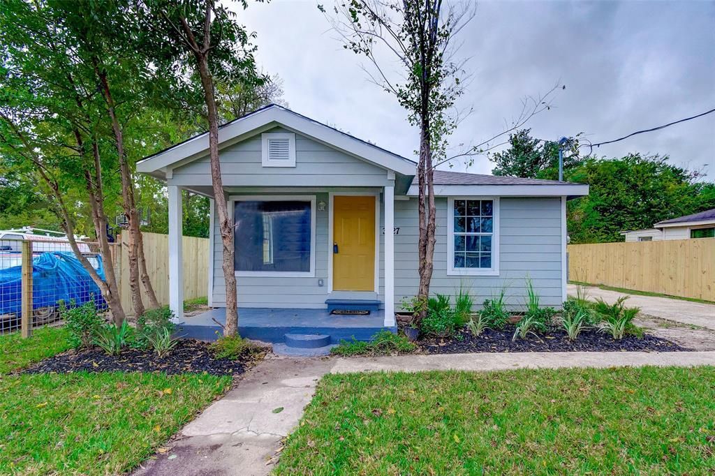A small white house with a yellow door and a porch surrounded by trees.