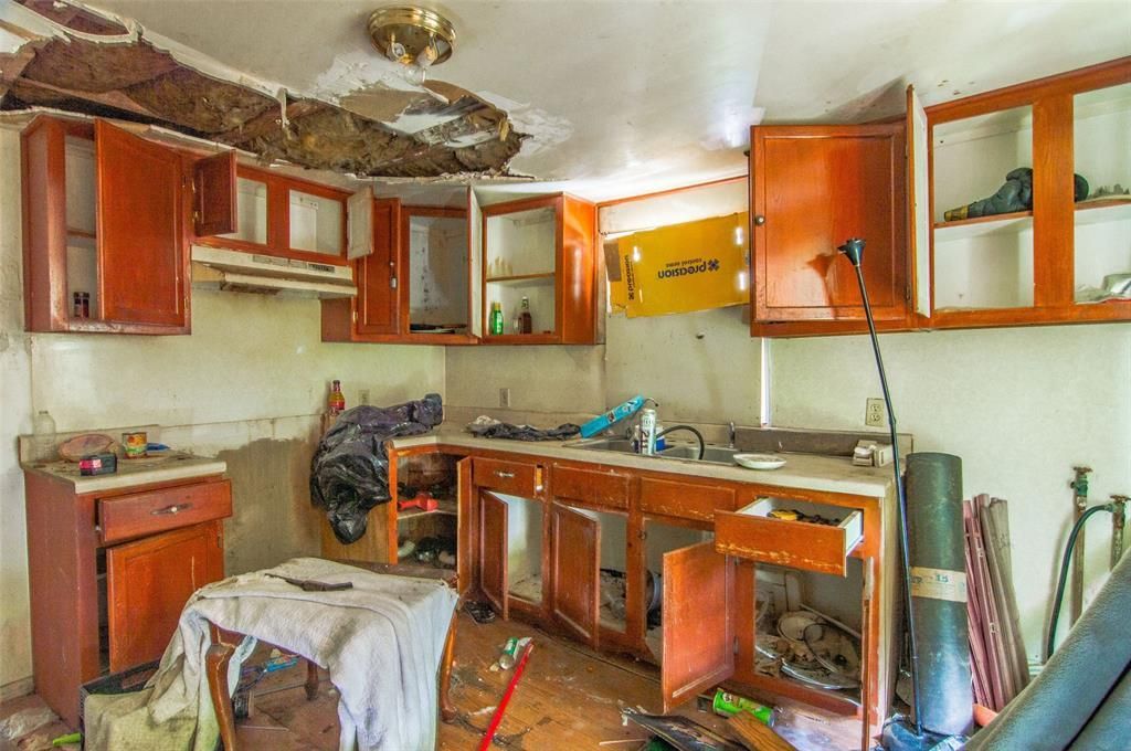 A kitchen in an abandoned house with a broken ceiling and a sink.