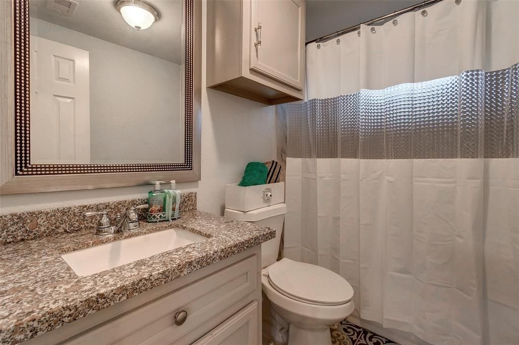 A bathroom with a toilet , sink , mirror and shower curtain.