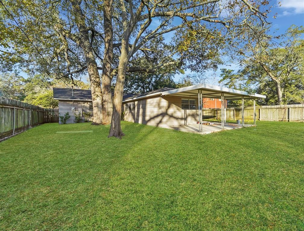 The backyard of a house with a large lawn and a carport.