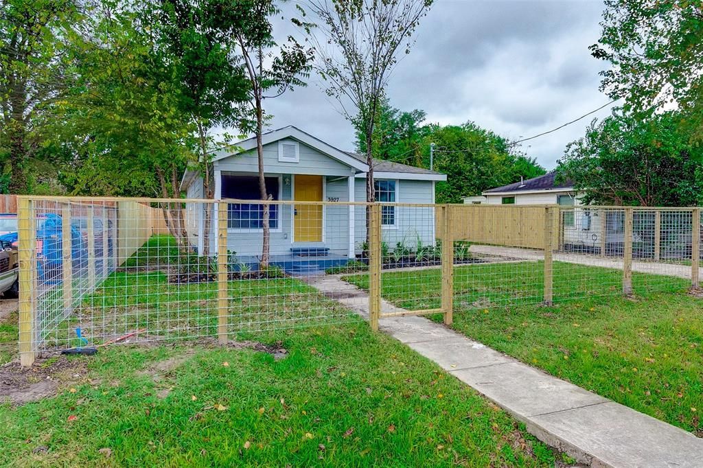 A house with a fence around it and a sidewalk in front of it.