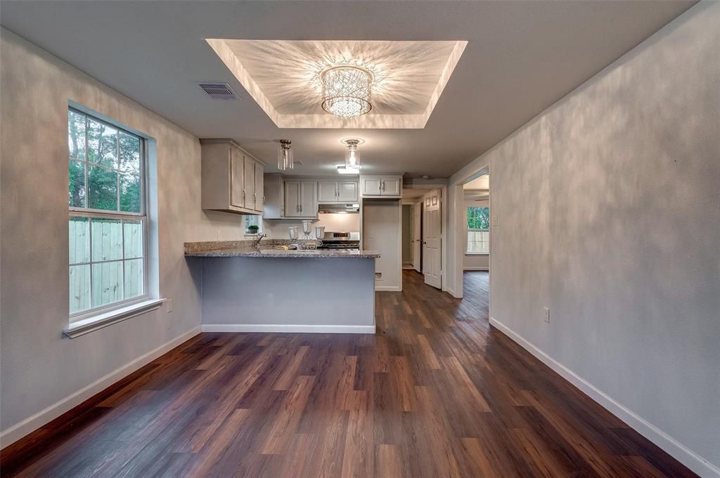 An empty room with hardwood floors and a kitchen in the background