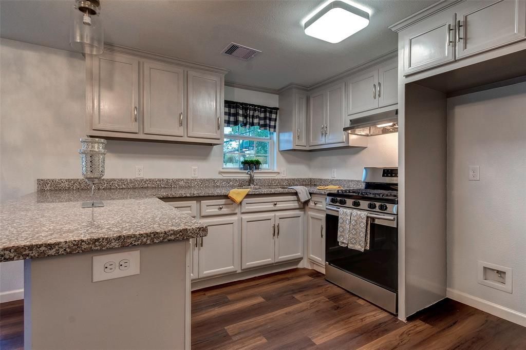 A kitchen with white cabinets , granite counter tops , stainless steel appliances and hardwood floors.