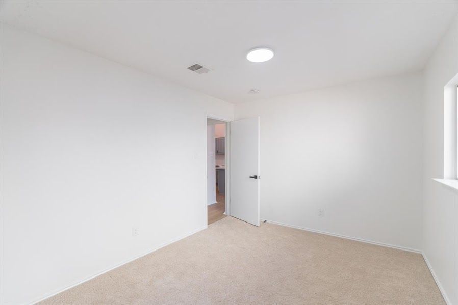 An empty bedroom with white walls and a tan carpet.