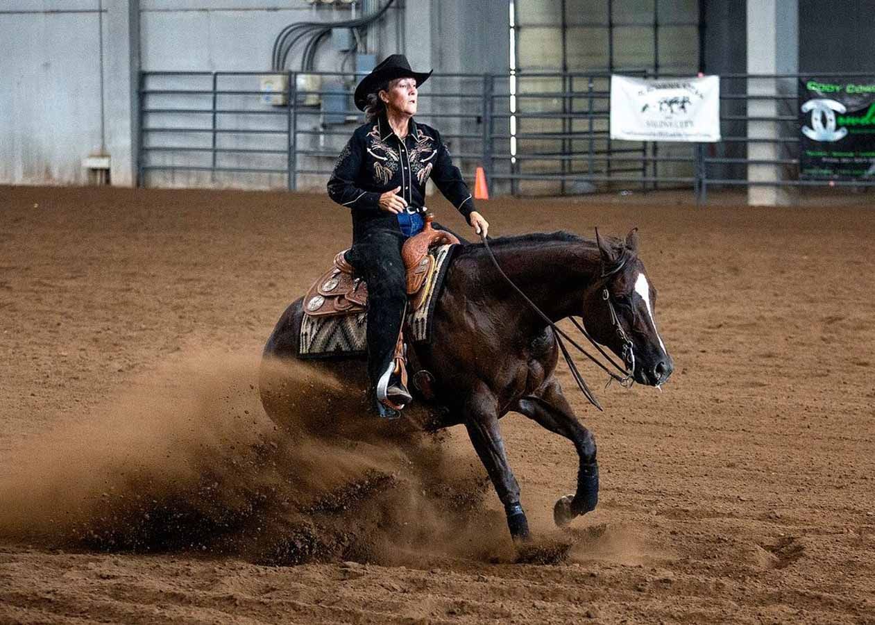 Cowgirl on a dark horse sliding through a dirt arena, kicking up dust during a rodeo run