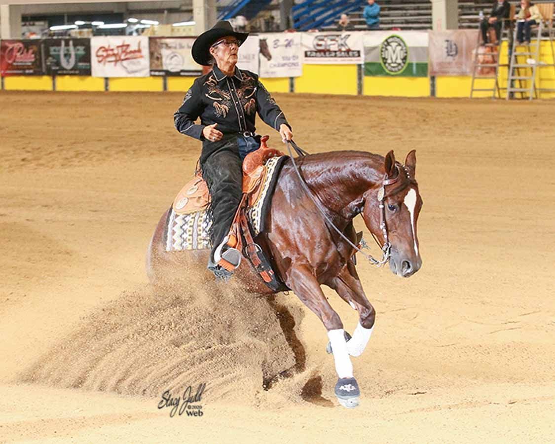 Cowboy riding a brown horse in an indoor arena, kicking up dirt during a fast turn.
