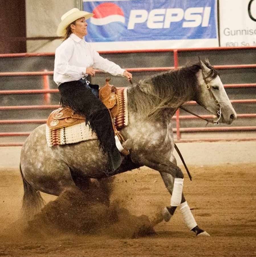 Cowboy riding a gray horse at a rodeo arena, kicking up dust