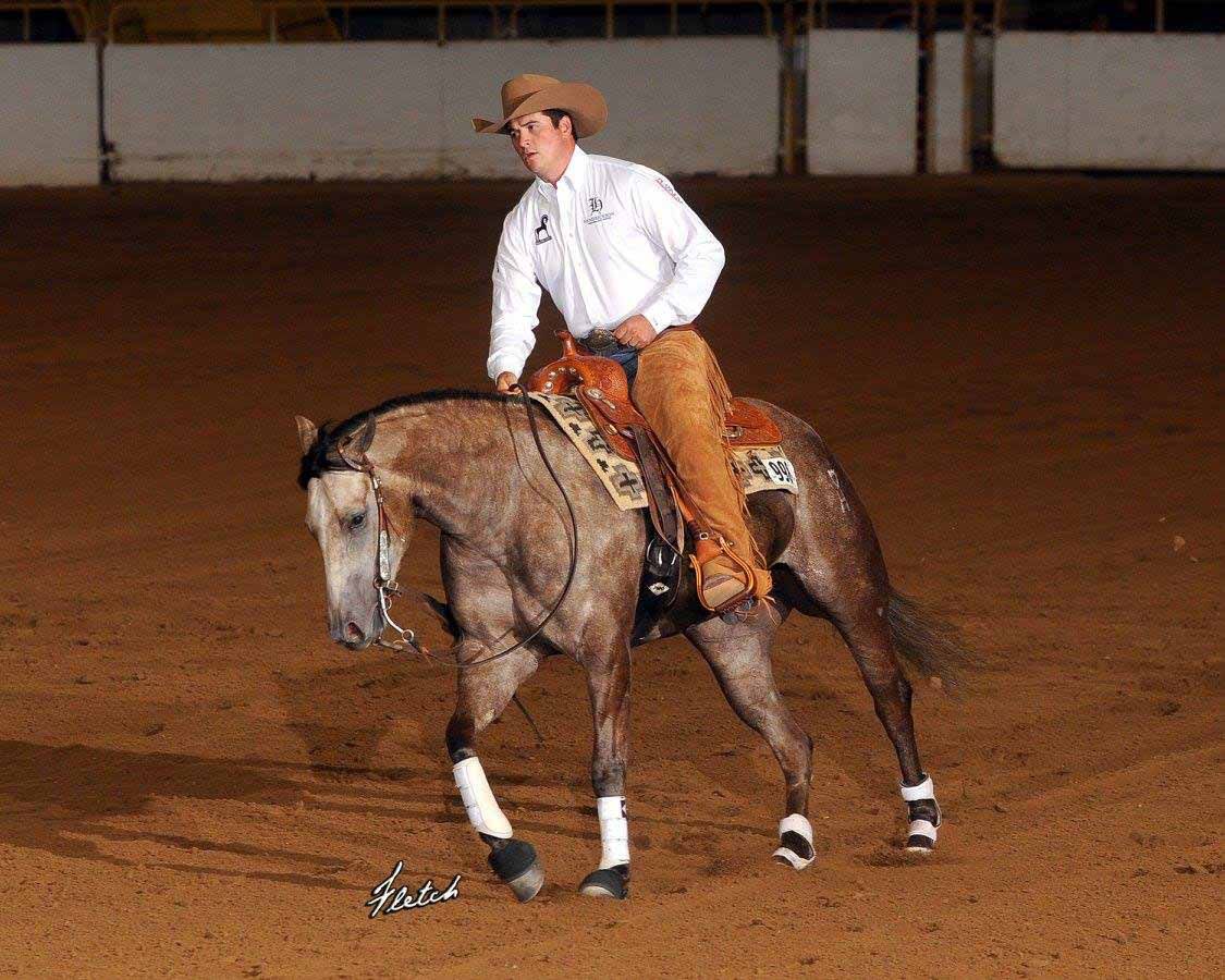 Cowboy riding a horse in an indoor arena, horse walking on reddish dirt.