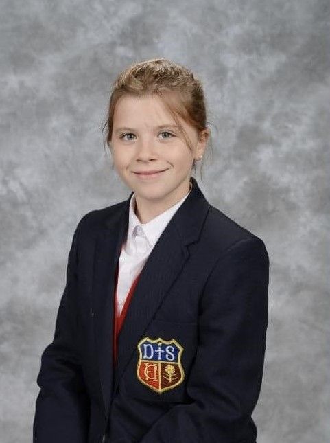 A young girl wearing a dhs jacket stands in front of a grey background