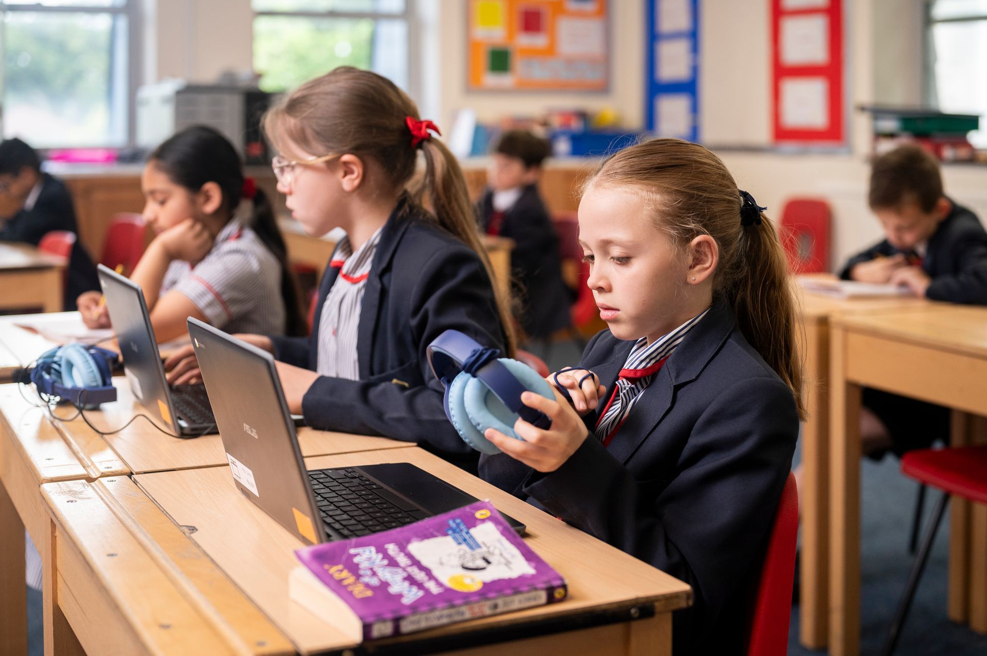 A group of children are sitting at desks in a classroom using laptops.