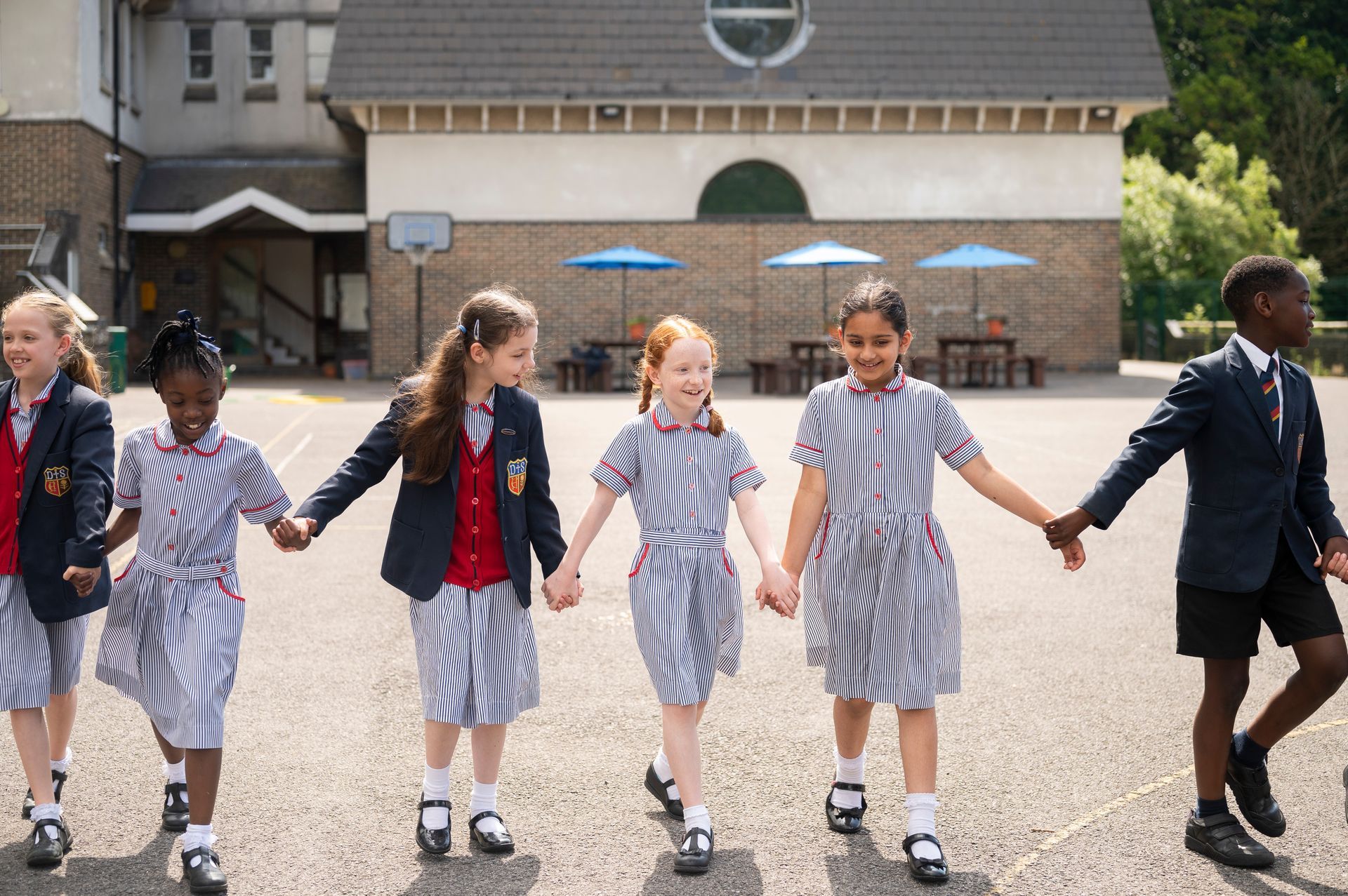 A group of children in school uniforms are holding hands and walking in a line.