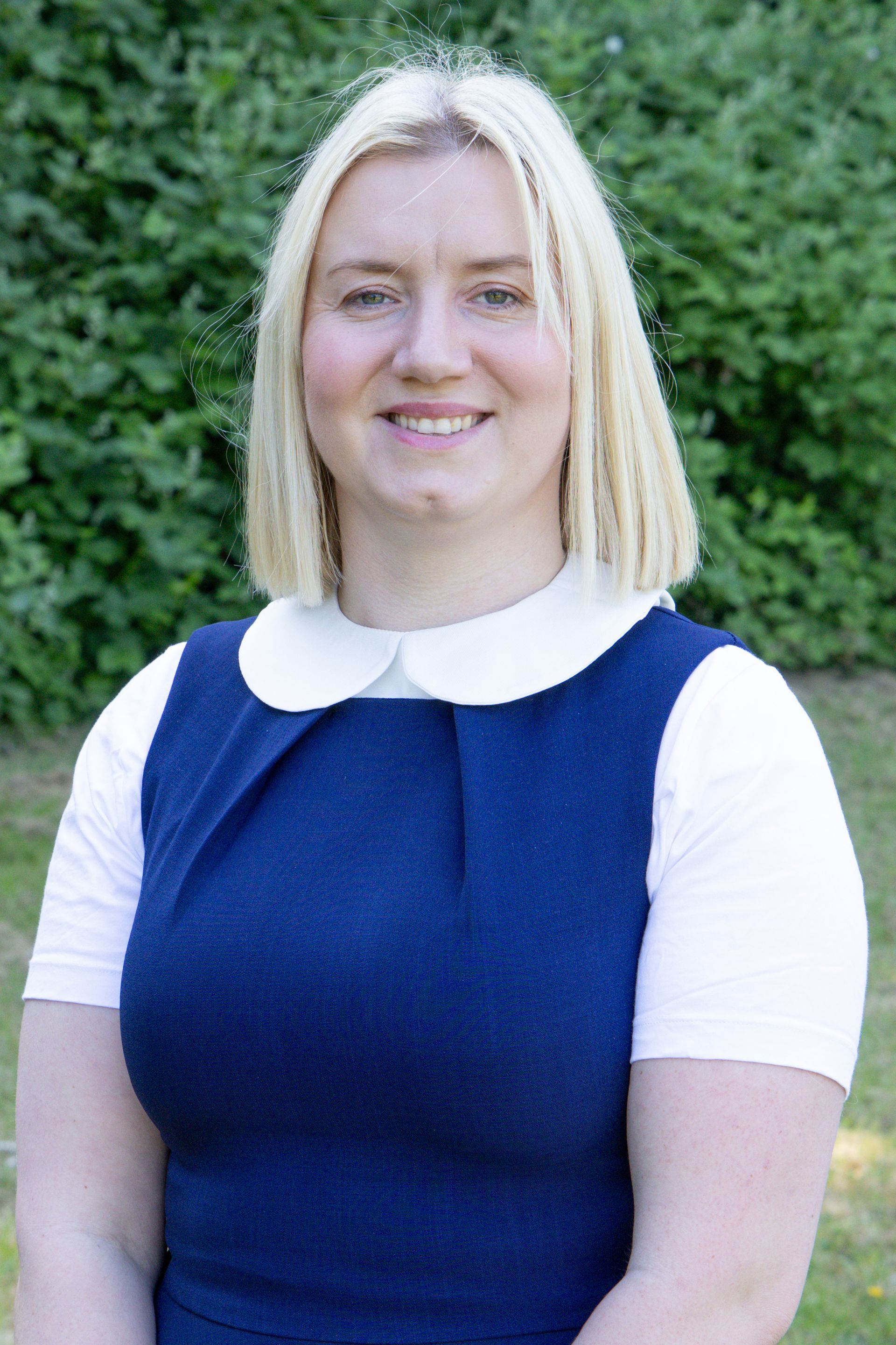 A woman in a blue dress and white shirt is smiling for the camera.