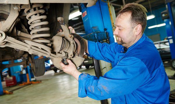 A Man Is Working On The Suspension Of A Car In A Garage — Tamworth Muffler Man In Tamworth, NSW
