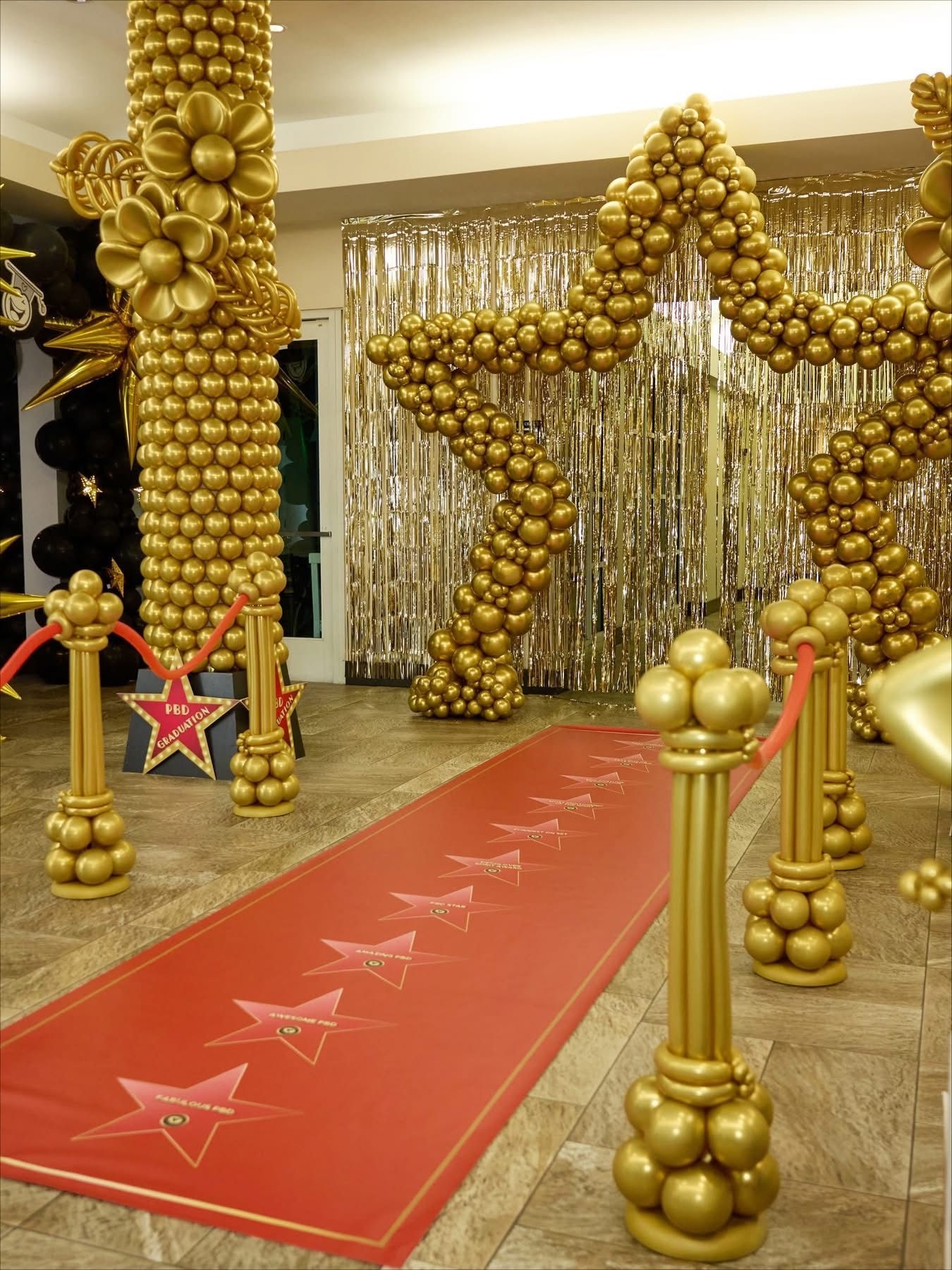 Gold balloon arch and columns framing a red carpet with stars in an elegant indoor event venue