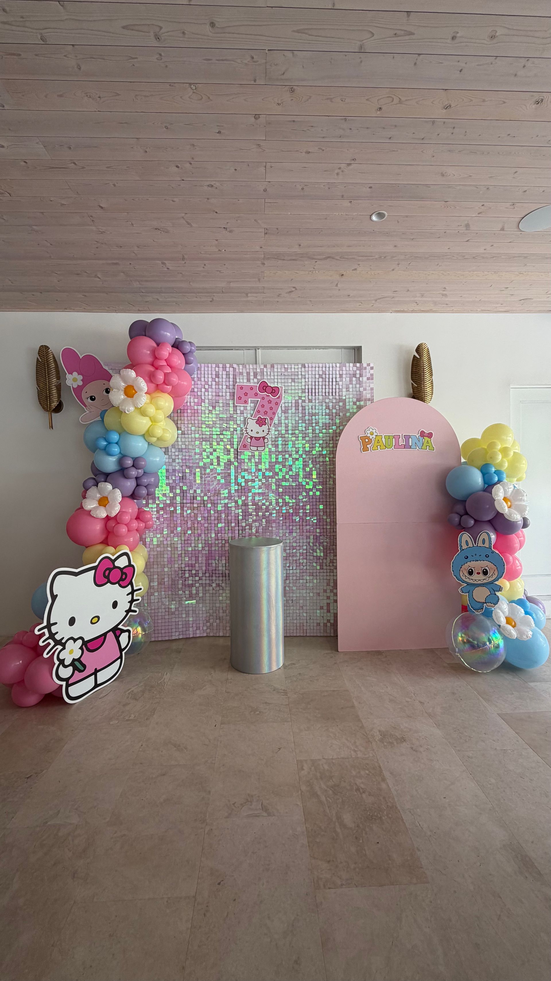 Pink birthday party backdrop with colorful balloon garlands, Hello Kitty decor, and a silver cylindrical stand