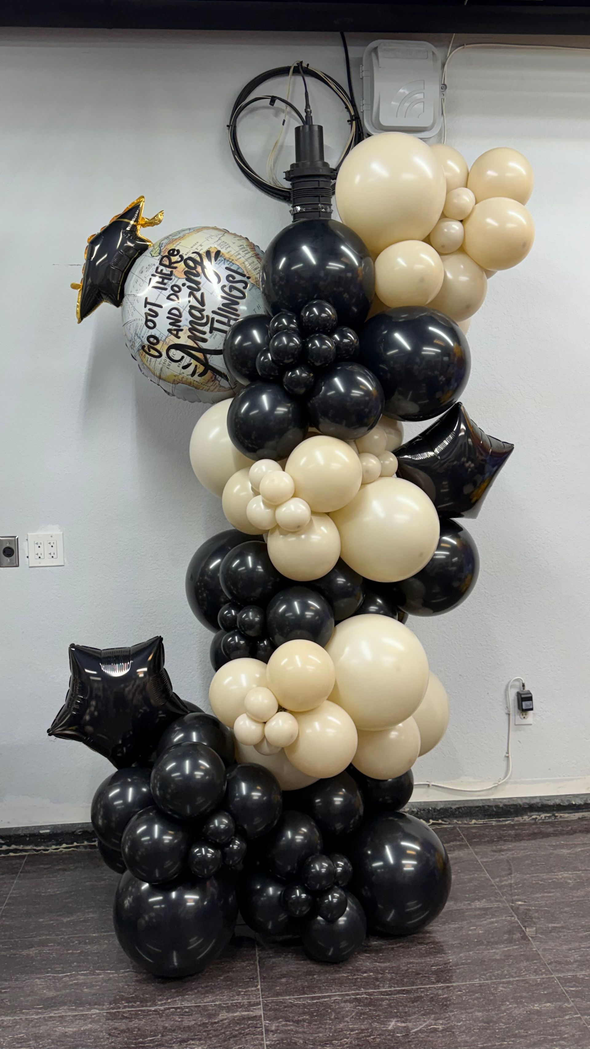 Black, cream, and gold balloon columns with star balloons in a lobby, with a clock on the wall above