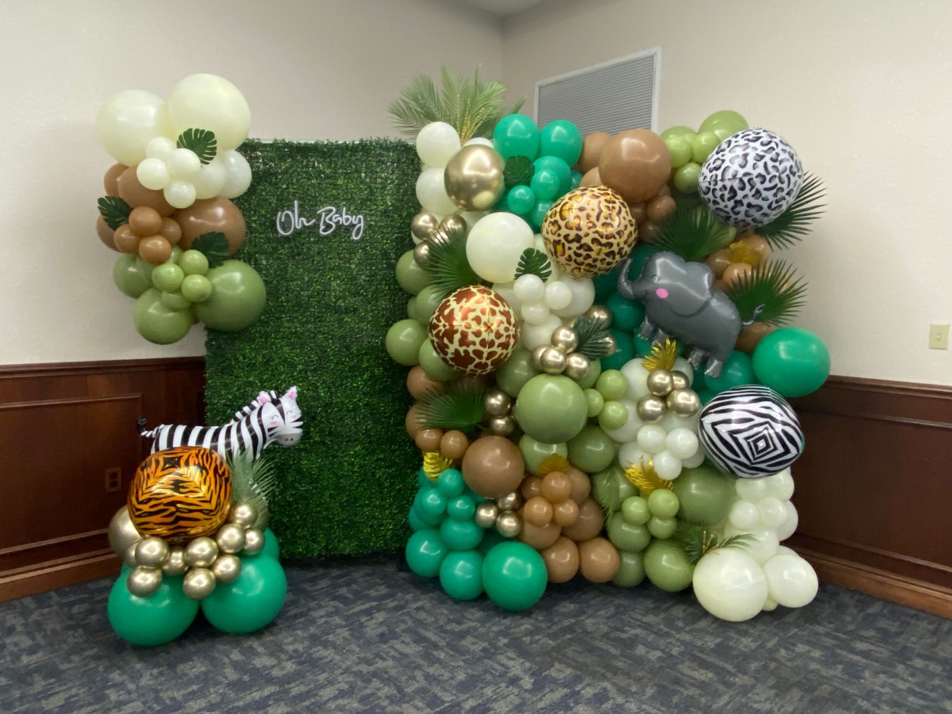 Green, gold, and white balloon safari display with animal balloons and zebra props on a backdrop wall