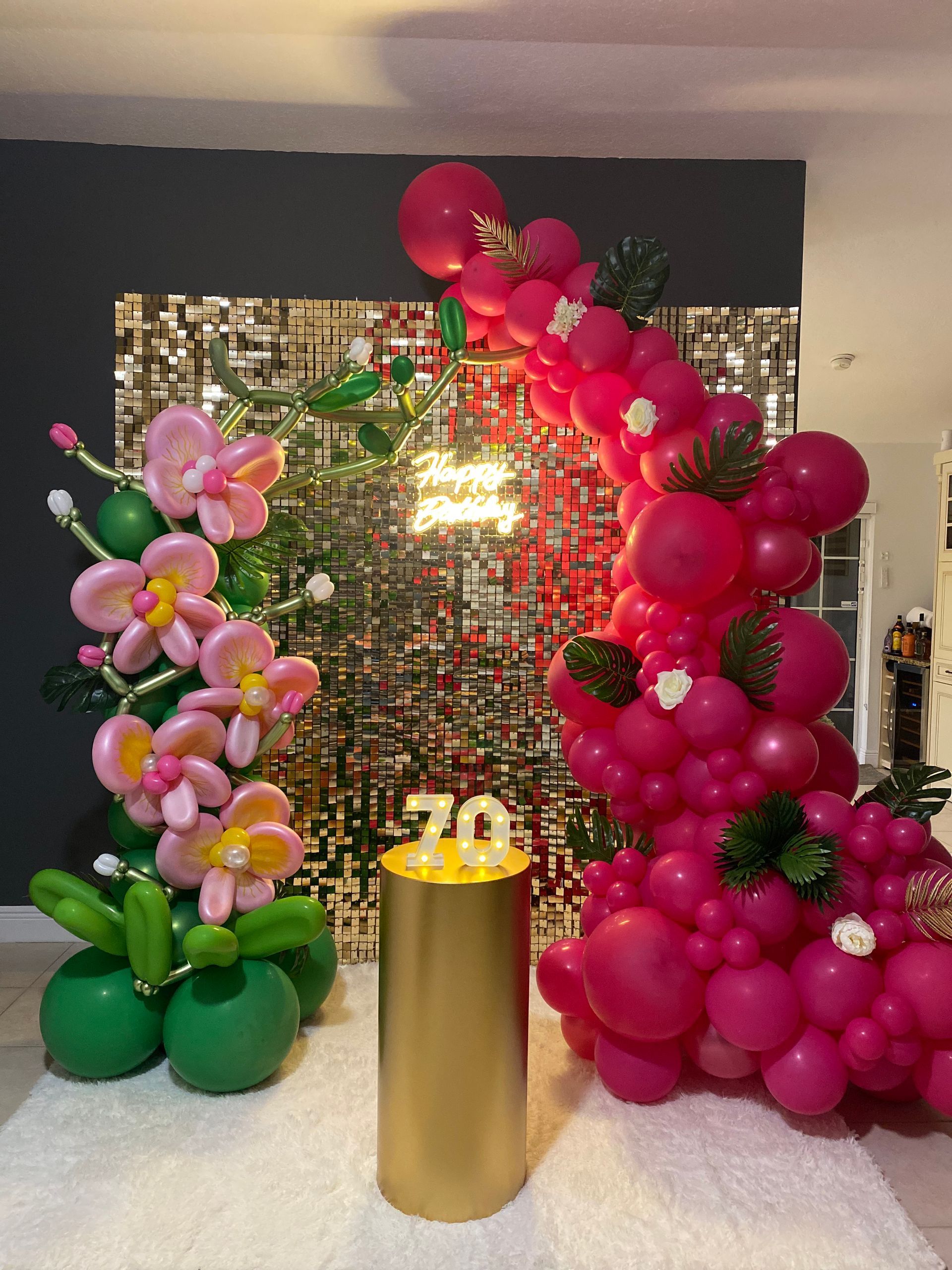 Balloon floral display in pink and green around a gold pedestal in a decorated indoor event space