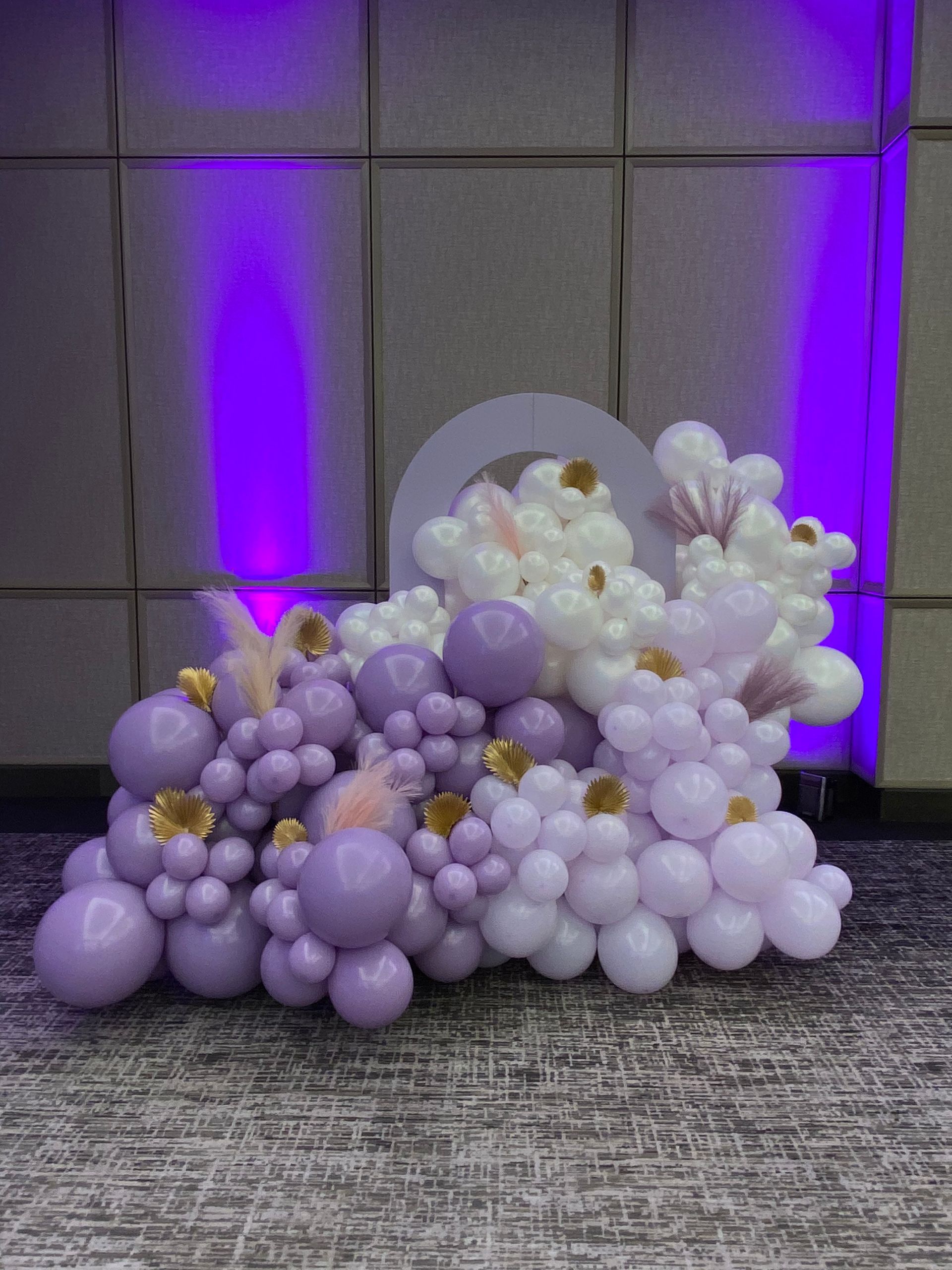 Lavender, white, and pearl balloon arrangement with flowers against a purple-lit backdrop
