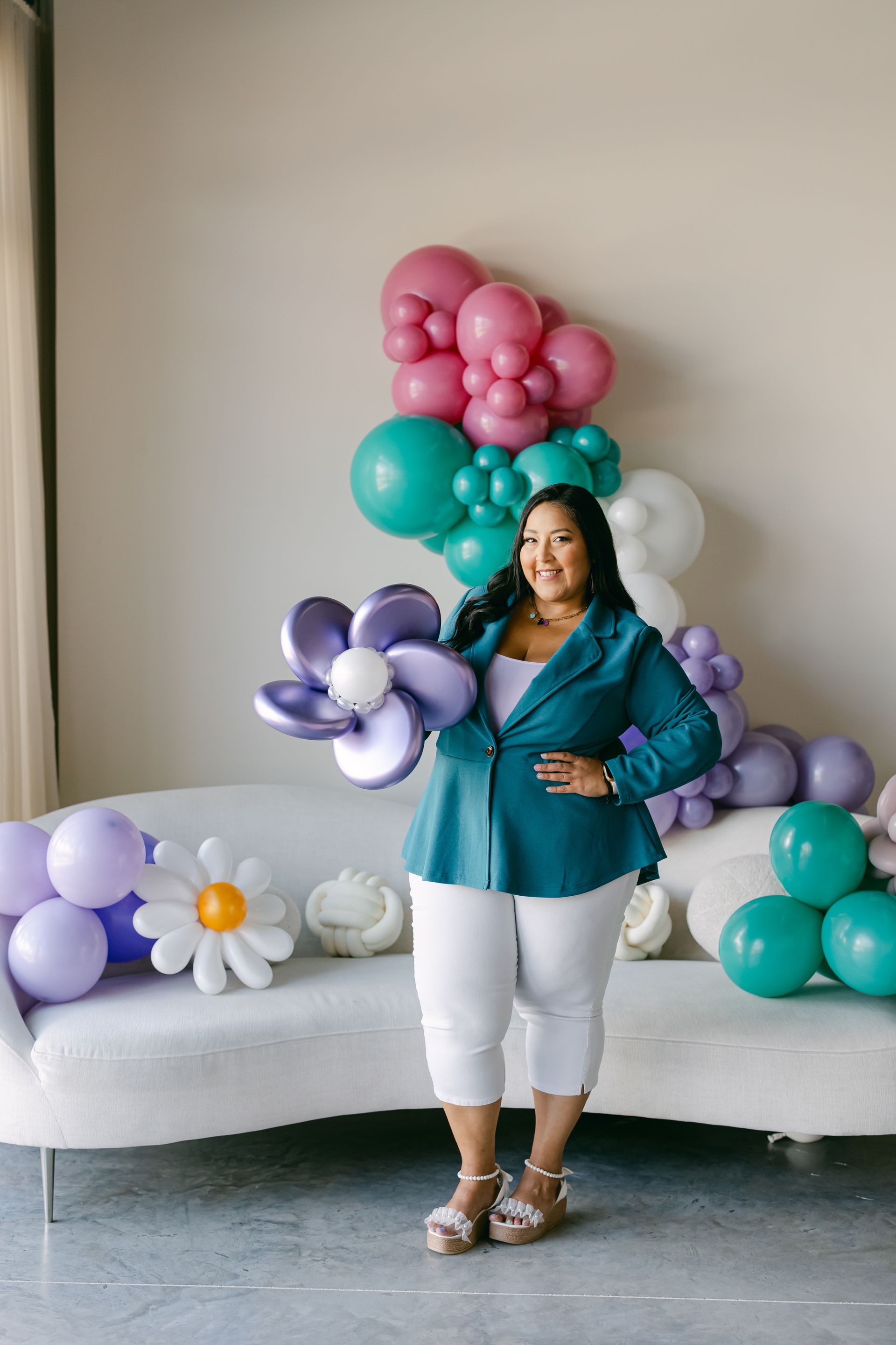 Woman posing in teal top before balloon flower display and white bench backdrop