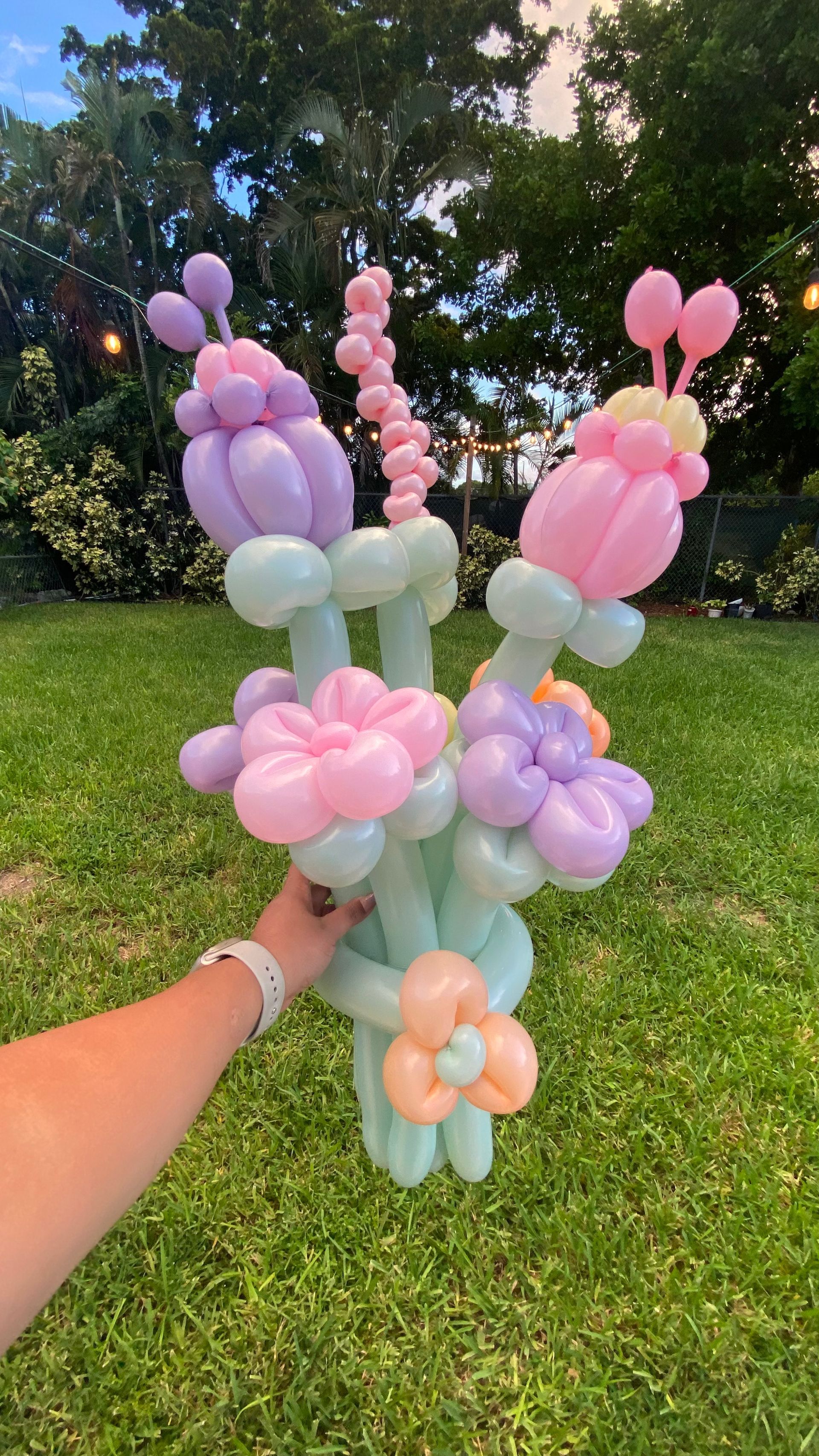 Pastel balloon flower bouquet held outdoors on a grassy lawn with trees in the background