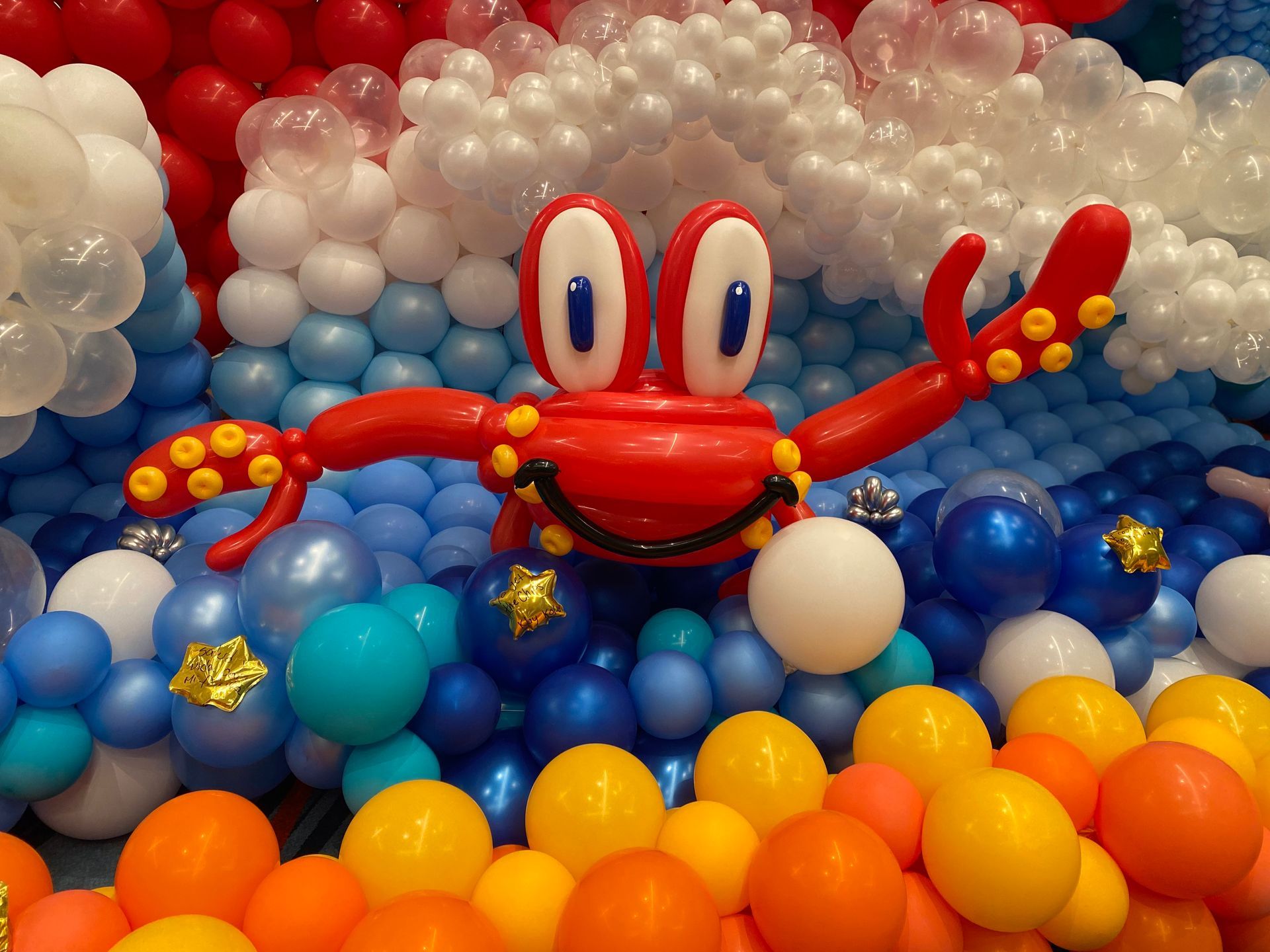 Red cartoon crab with outstretched claws amid colorful balloons in a festive display