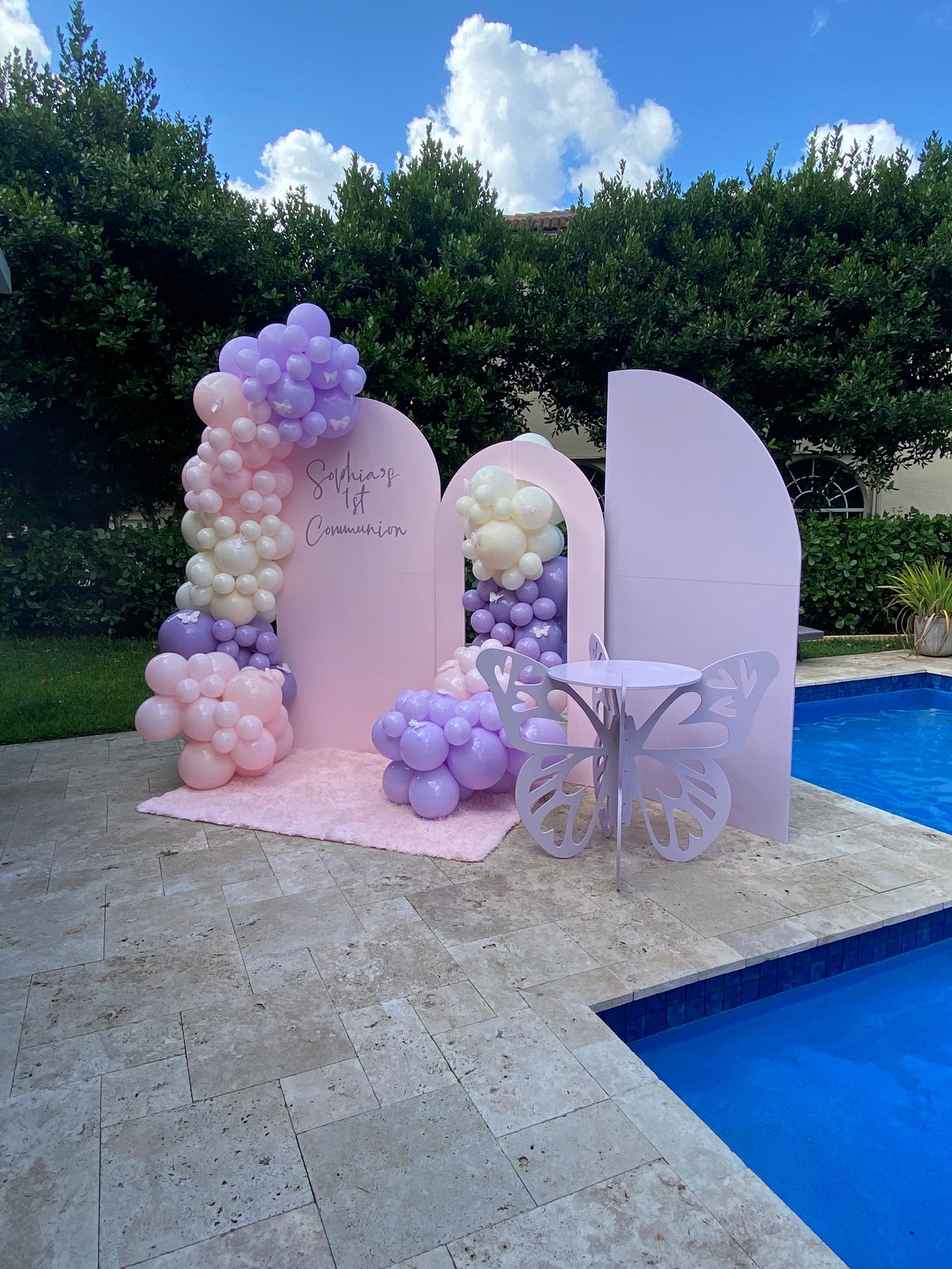 Pastel balloon arch and archway beside a pool on a pink platform outdoors