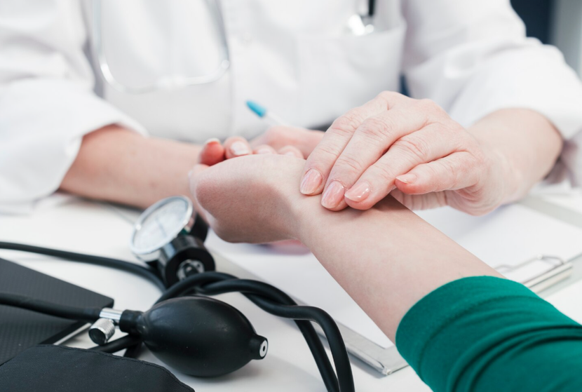 Médico examinando la muñeca de un paciente con un manguito de presión arterial cerca.