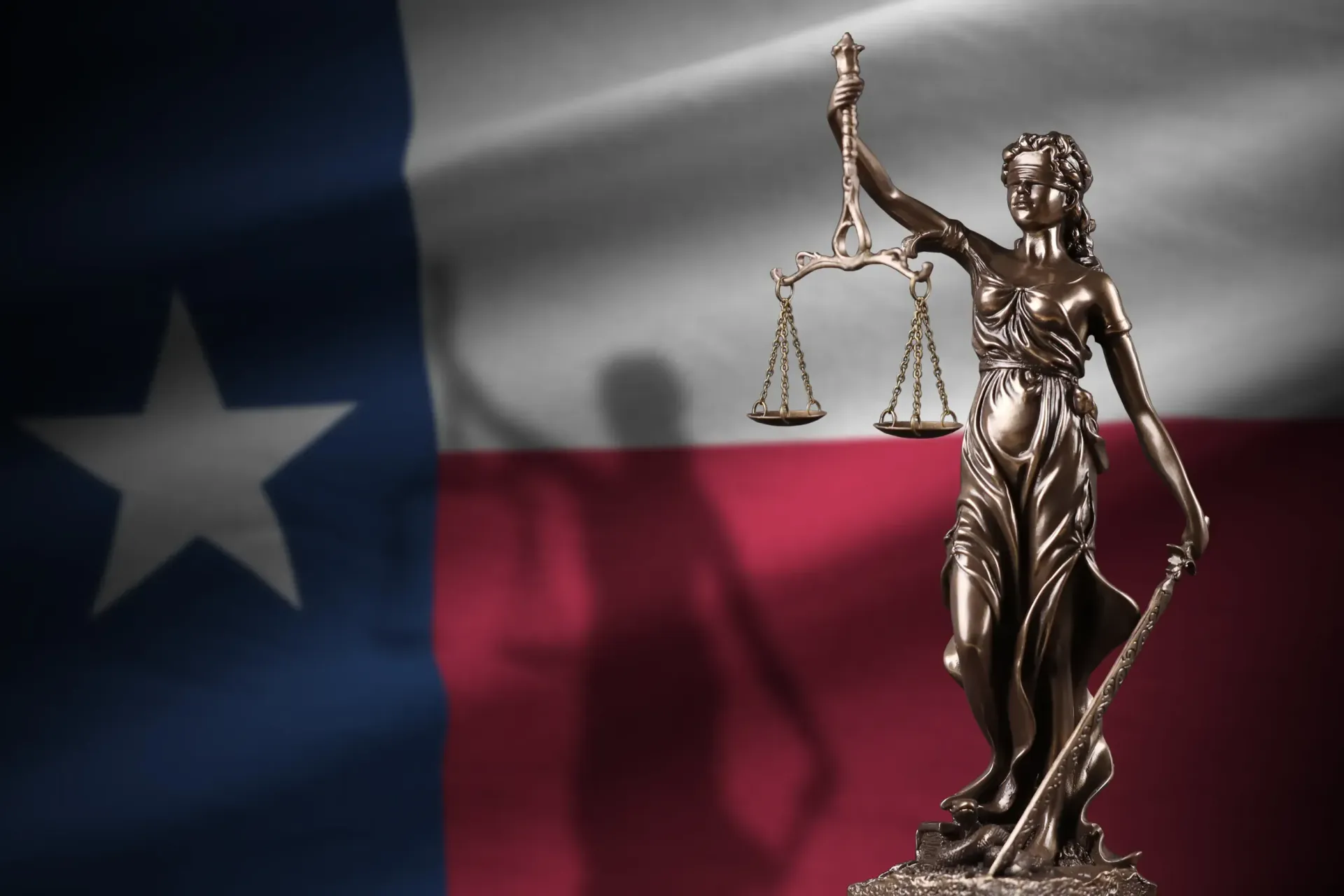 Texas flag behind a bronze Lady Justice statue holding scales