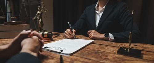 Lawyer and client across a desk signing documents in a dim office