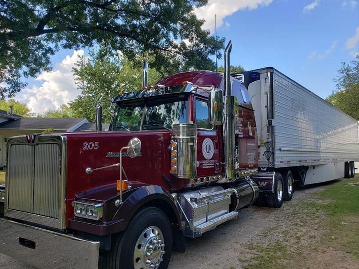 A red semi truck is parked next to a white trailer.