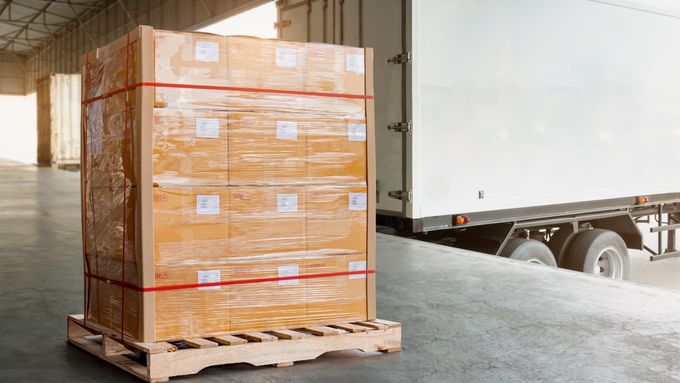 A stack of boxes on a wooden pallet in front of a truck in a warehouse.