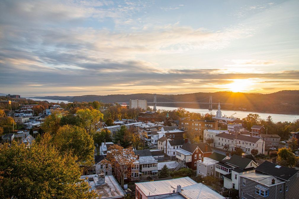 Sunset over a coastal cityscape with water, hills, and autumn trees in the foreground Sunset over a coastal cityscape with water, hills, and autumn trees in the foreground