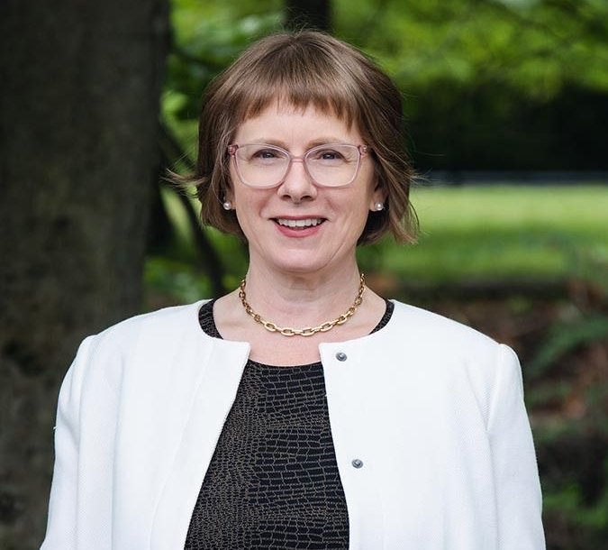Portrait of a smiling woman in glasses and a white blazer outdoors, with a blurred green background Portrait of a smiling woman in glasses and a white blazer outdoors, with a blurred green background