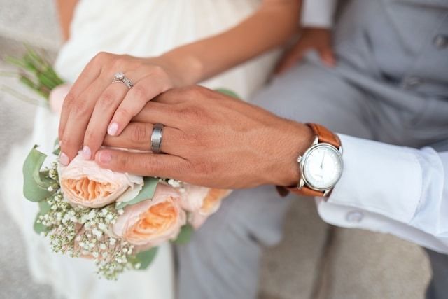 Hands with wedding rings resting on a bouquet of peach roses and white flowers