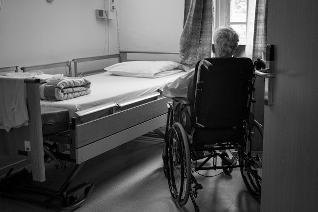 Person in a wheelchair beside a hospital bed in a black-and-white room