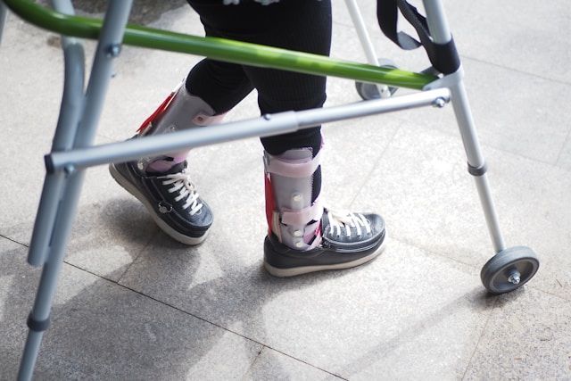 Lower legs using a green walker, wearing black sneakers and patterned socks on a tiled floor.