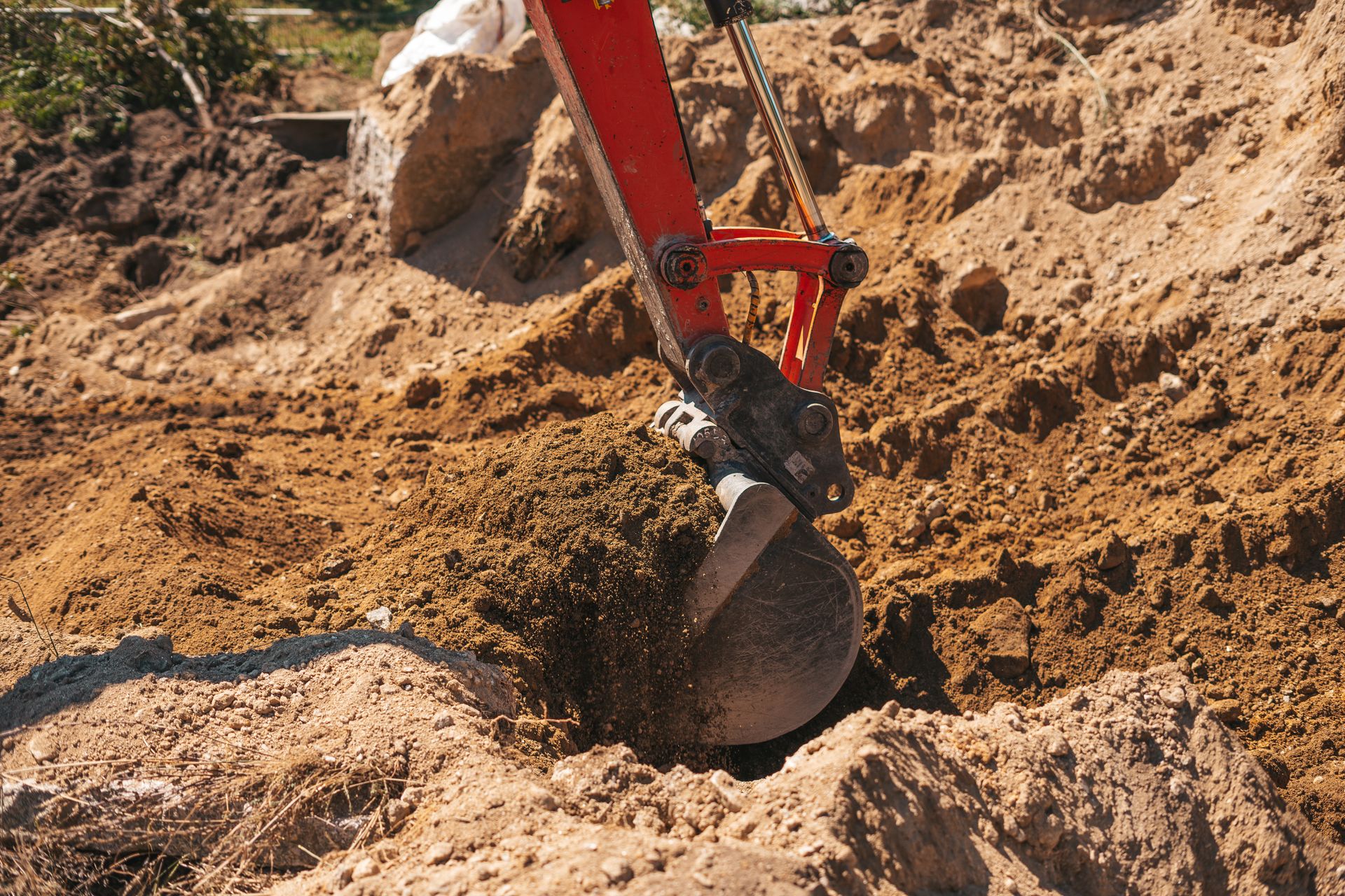 Excavator bucket digging into a pile of sandy soil at a construction site