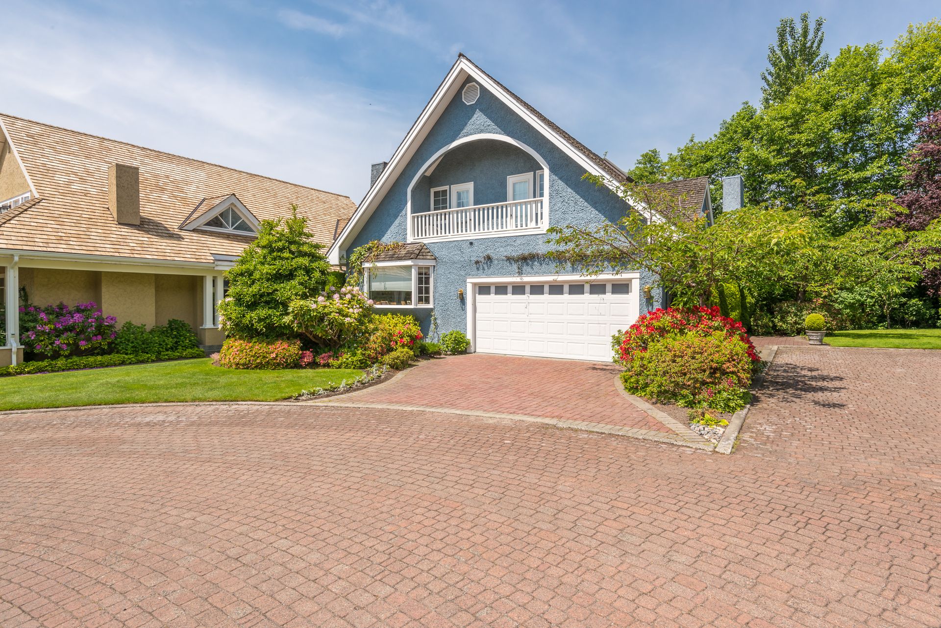 Suburban house with blue gable, white garage, and brick driveway under a clear sky