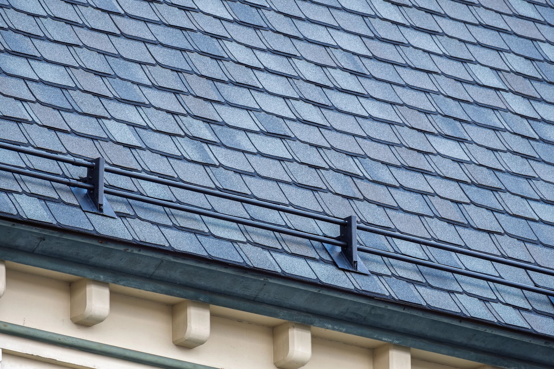 Slate roof with two black brackets and a row of white eaves against a blue-gray background