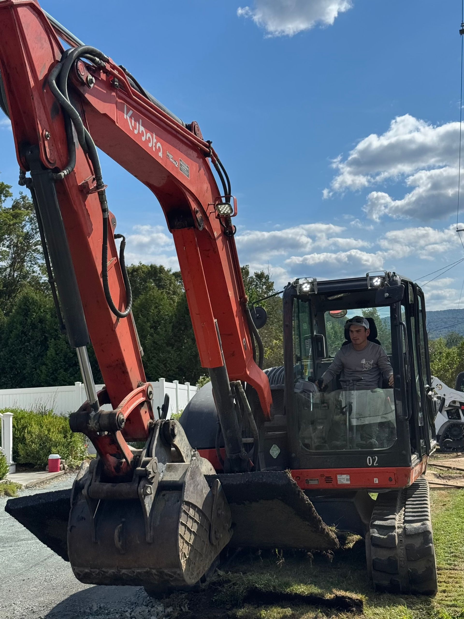 Red excavator on a dirt road with a person in the cab under a cloudy blue sky