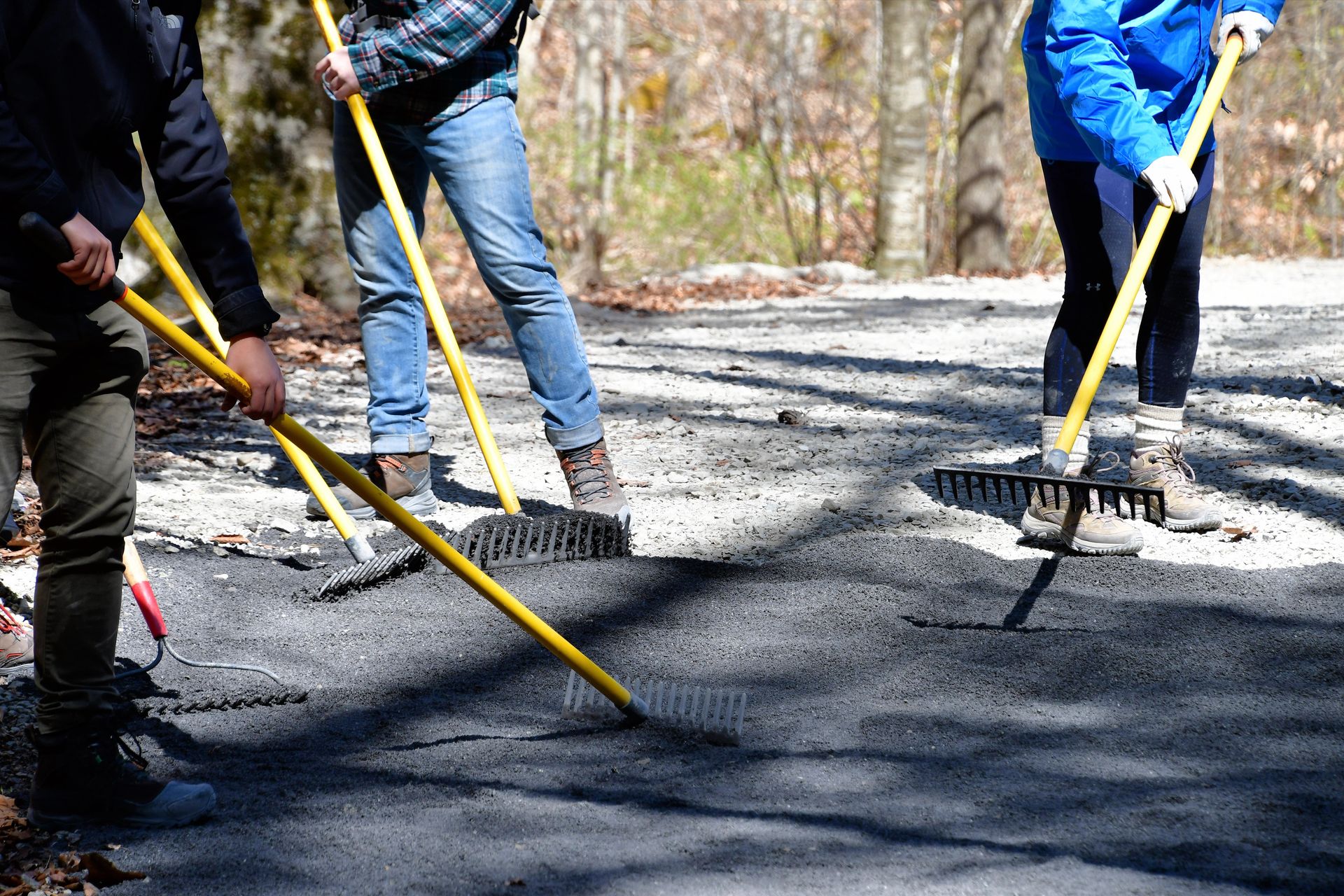 Workers spreading gravel on a road with rakes and shovels outdoors