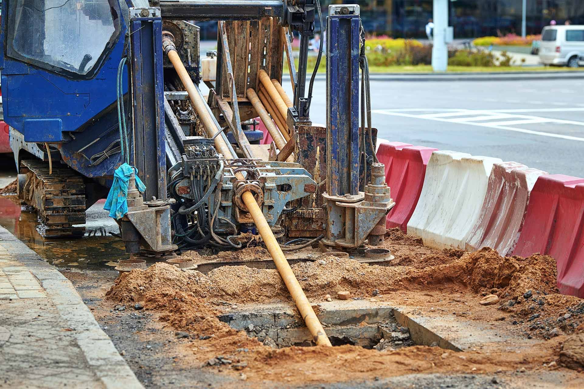 Drilling machine on the street, excavating a hole, with barriers and traffic in the background