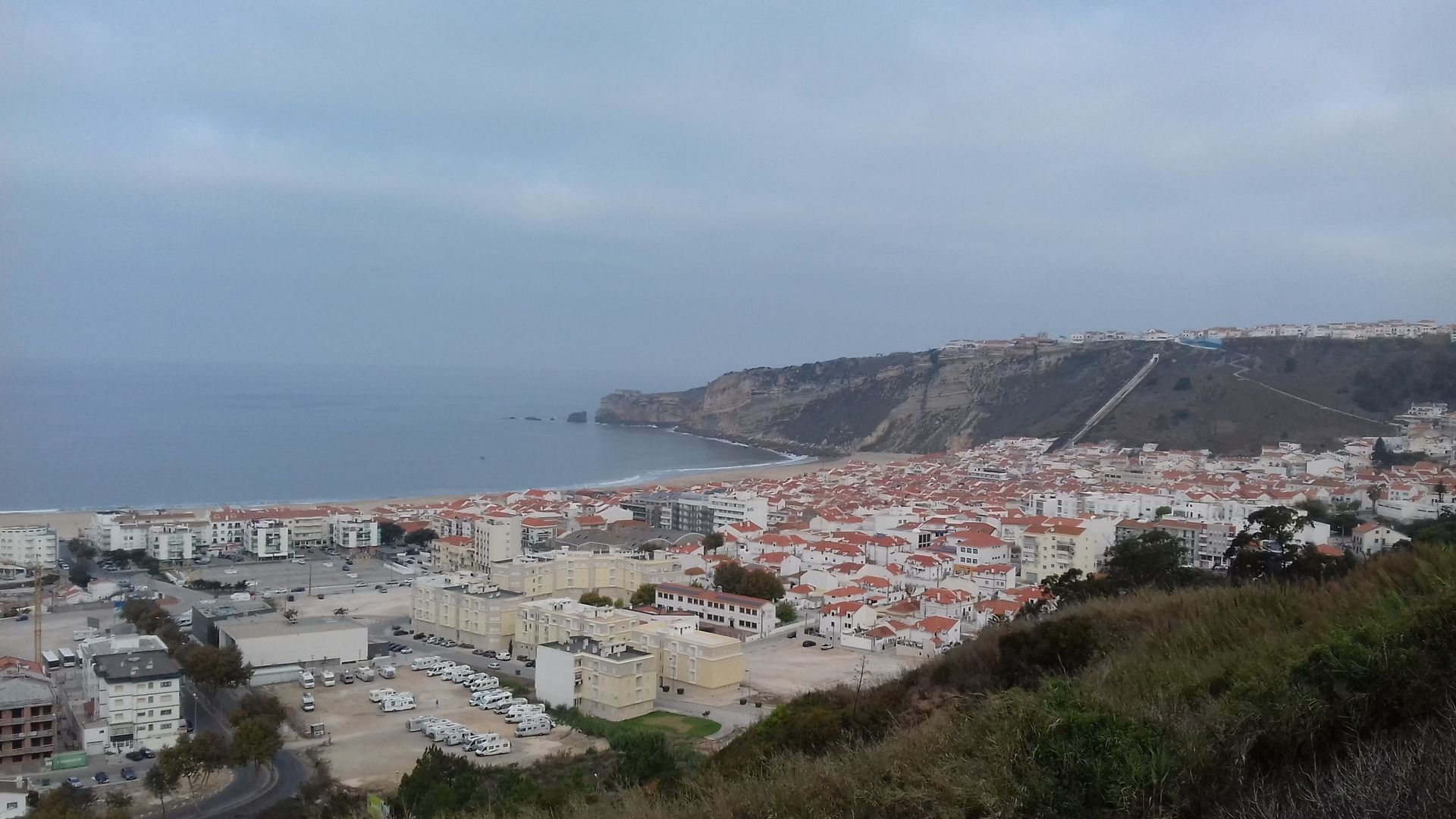 Coastal town with white buildings, red roofs, and a harbor under a cloudy sky