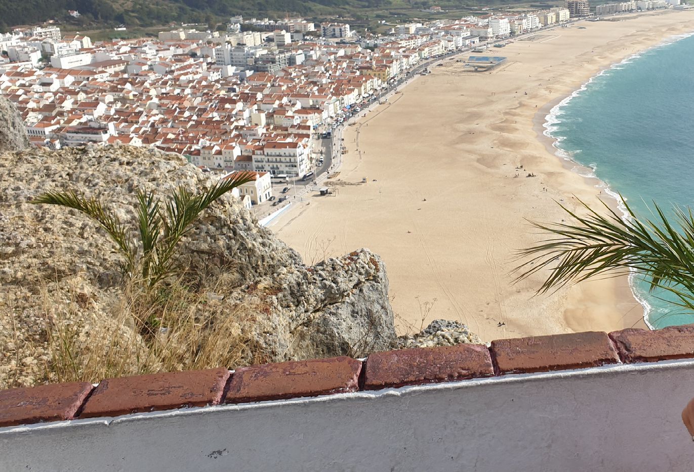 Panoramic view of a coastal town and sandy beach beside blue water, seen from a hilltop lookout