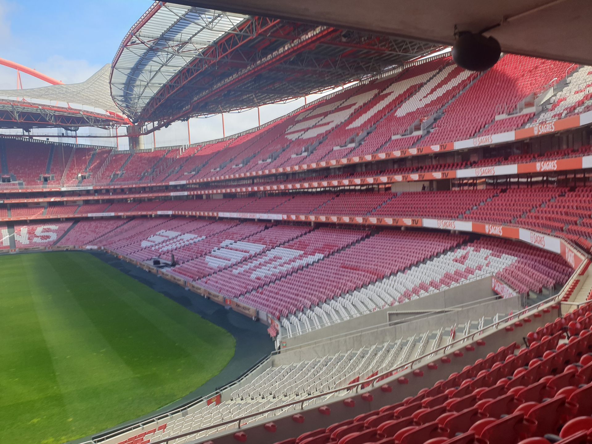 Empty red-and-white stadium stands with a green football pitch and arched roof
